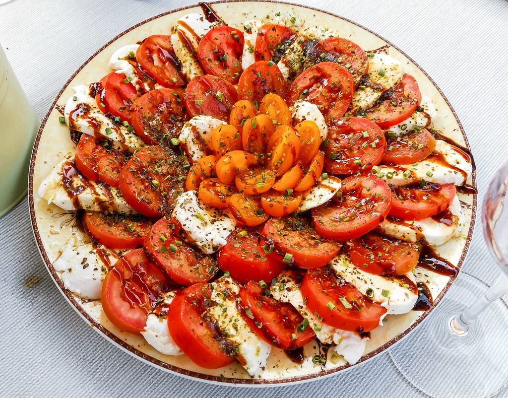 Wandbild Caprese Stillleben – Tomaten & Mozzarella Food Fotografie | Dieses ästhetische Food-Wandbild bringt ein Stück italienische Lebensfreude direkt in deine Räume. Das detailreiche Stillleben zeigt saftige Tomaten und zarten Mozzarella, kunstvoll abgerundet mit aromatischen Kräutern, frischem Basilikum und dunklem Balsamico-Essig auf einem rustikalen Teller. Ein moderner, hochwertiger Kunstdruck – ideal als Poster für die Küche, das Esszimmer oder stilvolle Cafés und Restaurants. - Realisiert mit Pictrs.com