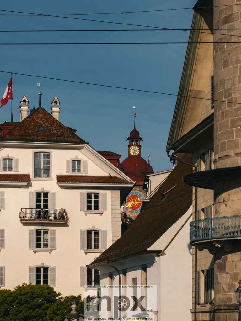 Luzerner Altstadt mit Zytturm und historischen Fassaden | Blick durch die Luzerner Altstadt auf historische Häuser, Dächer und den Zytturm mit Uhr, eingerahmt von Fassaden und Leitungen im warmen Licht. - Realisiert mit Pictrs.com
