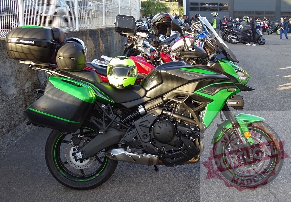 Kawasaki Versys 650 motorcycle parked near other motorcycles | Green Kawasaki Versys 650 motorcycle with helmets and side panniers parked near other motorcycles - Realized with Pictrs.com
