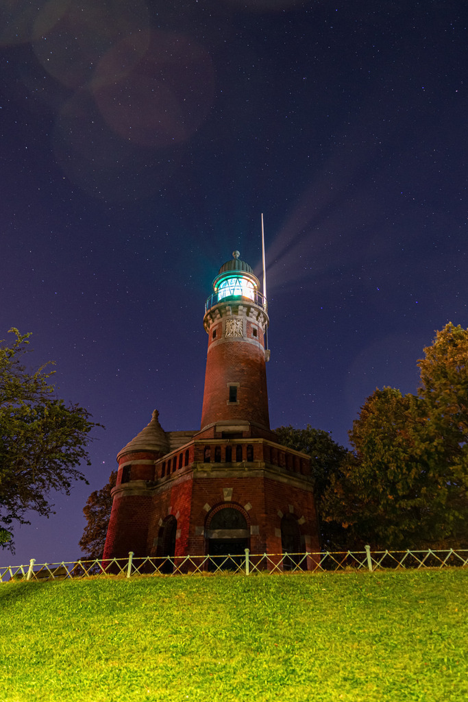 Leuchtturm Kiel Holtenau mit Sternenhimmel | Eine beeindruckende Nachtaufnahme des Leuchtturms Holtenau. Das Licht des Leuchtturms erzeugt einen hellen, sichtbaren Lichtstrahl, der sich in der Dunkelheit des Nachthimmels abzeichnet. Die Struktur des Turms ist im Kontrast zur Dunkelheit des Himmels und des umliegenden Geländes gut erkennbar. Das Leuchtfeuer des Holtenau-Leuchtturms weist Schiffen den sicheren Weg durch die Nacht und ist ein Zeichen der Hoffnung und des Schutzes in einer dunklen Umgebung. Es ist ein wundervolles Beispiel für die maritime Architektur und die Rolle, die Leuchttürme in der Geschichte der Seefahrt spielen.