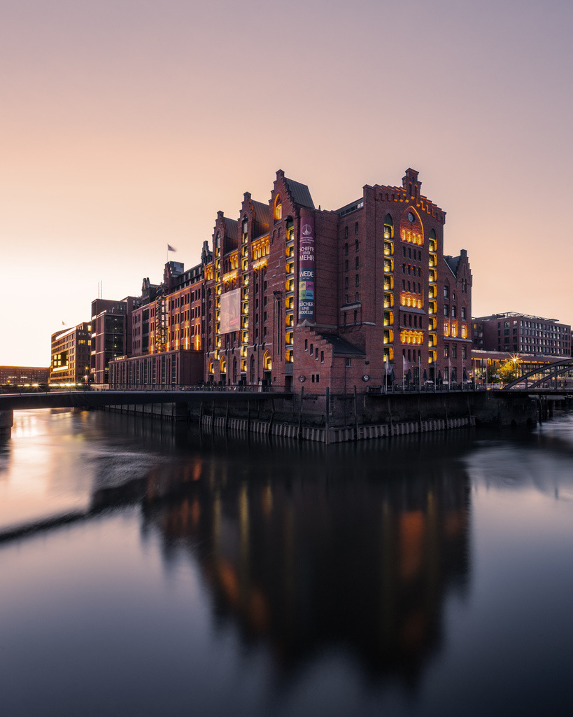 Spiegelung der Speicherstadt im Fleet | Ein historischer Speicherblock spiegelt sich während der blauen Stunde im ruhigen Wasser eines Hamburger Fleets. - Realisiert mit Pictrs.com