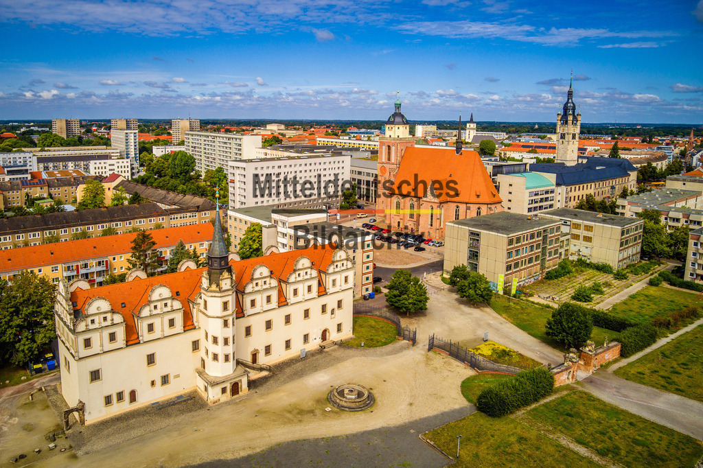 Stadtschloss und Marienkirche in Dessau-Roßlau -0023 | Dieses Luftbild zeigt das Stadtschloss Dessau und die Marienkirche im Zentrum von Dessau-Roßlau in Sachsen-Anhalt aus einer eindrucksvollen Vogelperspektive. Die beiden bedeutenden Bauwerke prägen das historische Stadtbild und gehören zu den bekanntesten Sehenswürdigkeiten der ehemaligen Residenzstadt an der Mulde.Im Mittelpunkt der Aufnahme steht das rekonstruierte Stadtschloss Dessau, das an die lange Geschichte der anhaltischen Residenz erinnert. Über viele Jahrhunderte war Dessau das politische und kulturelle Zentrum des Fürstentums und späteren Herzogtums Anhalt. Die markante Architektur des Schlosses bildet gemeinsam mit den umliegenden Plätzen und Straßenzügen einen wichtigen Bestandteil des Stadtzentrums.Unweit des Schlosses erhebt sich die Marienkirche mit ihren charakteristischen Türmen über die Dächer der Innenstadt. Das historische Gotteshaus zählt zu den bedeutendsten Sakralbauten der Stadt und prägt seit Jahrhunderten die Silhouette Dessaus. Aus der Vogelperspektive werden die harmonischen Proportionen der Kirche und ihre Einbettung in das urbane Umfeld besonders deutlich sichtbar.Dieses Luftbild verbindet Geschichte, Architektur und Stadtentwicklung und zeigt das Herz der Bauhausstadt Dessau-Roßlau aus einer außergewöhnlichen Perspektive hoch über den Dächern Sachsen-Anhalts. - Realisiert mit Pictrs.com