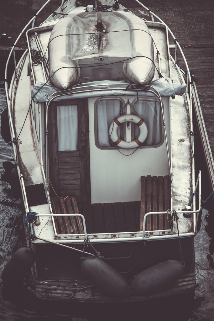 Silent Harbor | Ein stiller Moment im Hafen: Diese Detailaufnahme zeigt ein fest vertäutes Motorboot aus der Vogelperspektive. Gebrauchsspuren, verwittertes Holz und die sanften Bewegungen des Wassers erzählen von vergangenen Reisen und ruhigen Tagen am Kai. Die dezente Farbgebung und die klare Komposition verleihen dem Motiv eine zeitlose, maritime Atmosphäre zwischen Nostalgie und Gelassenheit. - Realisiert mit Pictrs.com