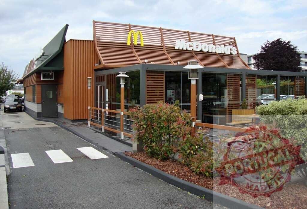McDonald's fast food restaurant building with drive-thru signage | Modern McDonald's fast food restaurant showing its exterior architecture and golden arches on a cloudy day - Realized with Pictrs.com