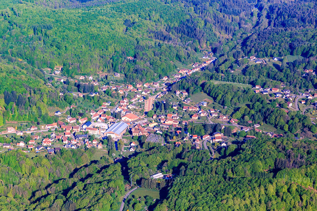 Vue aérienne: Vue d'ensemble de la ville le matin depuis le sud-est, incluant le théâtre Halle Verrière et le Centre international d'art verrier. à Meisenthal dans le département Moselle, France. Photo: IMG_146050.jpg prise le 01/05/2025 par Werner Riehm/FLY-FOTO.eu – Résolution de l'original: 5472 x 3648 px