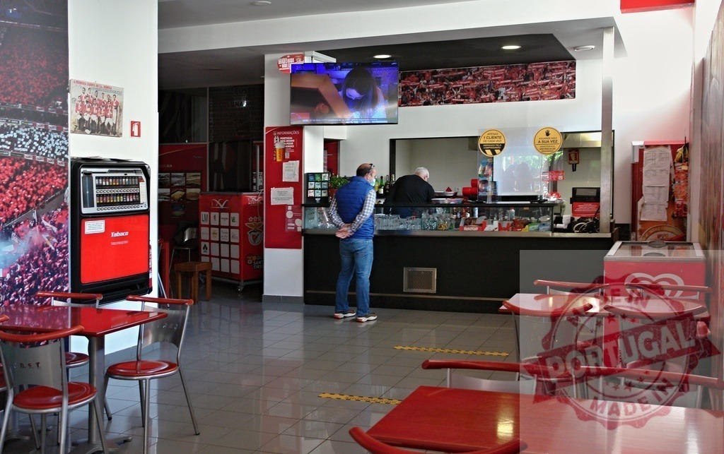People at SL Benfica snack bar interior | People standing and serving at a snack bar counter with red furniture - Realized with Pictrs.com