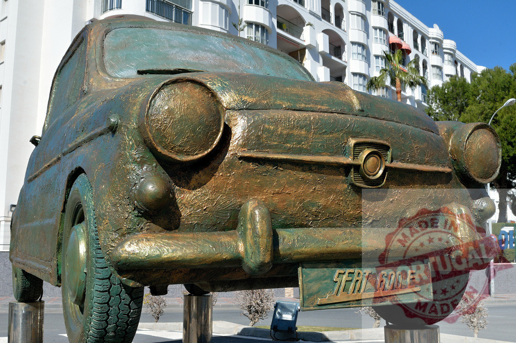 Monument of a vintage Seat 600 car celebrating spanish automotive history | Close-up of a weathered bronze Seat 600 sculpture commemorating Spain's iconic car in front of a modern building - Realisiert mit Pictrs.com