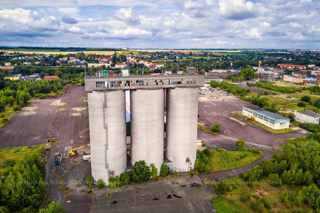 Magdeburg_Industrie_Fahlberg_List_3_Silos-0008 | Salbke und Westerhüsen sind Stadtteile, deren Entwicklung über Generationen eng mit der Industrie verbunden war. Große Fabrikanlagen, technische Bauwerke und weitläufige Gewerbeflächen gehörten lange zum Alltag. Die drei markanten Hochsilos auf dem ehemaligen Fahlberg-List-Gelände waren ein weithin sichtbares Zeichen dieser Vergangenheit.  –  –  Die Silos entstanden 1959/60 nahe der Elbe und dienten der Lagerung von Apatit, einem Rohstoff für die Düngemittelproduktion. Über Jahrzehnte prägten sie die Silhouette des Magdeburger Südostens. Für viele Menschen aus der Umgebung waren sie ein vertrauter Anblick auf dem Weg durch ihren Stadtteil – ein Stück Industriegeschichte, das selbstverständlich zum Landschaftsbild gehörte.  –  –  Im Juli 2024 begann der Abriss der drei Betonsilos. Dieses Luftbild entstand nur eine Woche zuvor. Es hält damit einen besonderen Moment fest: Die Bauwerke stehen noch, doch ihr Ende ist bereits besiegelt. Kurz darauf verschwand eine Landmarke, die Salbke und Westerhüsen über Jahrzehnte mitgeprägt hatte.  –  –  Solche Aufnahmen sind für mich mehr als ein Blick von oben. Sie bewahren Orte, die sich verändern oder ganz verschwinden. Wer im Magdeburger Süden aufgewachsen ist oder hier gelebt hat, verbindet mit solchen Bauwerken vielleicht eigene Erinnerungen an die Arbeitswelt, den Alltag und das Gesicht des Stadtteils. So bleibt ein Stück Magdeburger Industriegeschichte im Bild erhalten. - Realisiert mit Pictrs.com