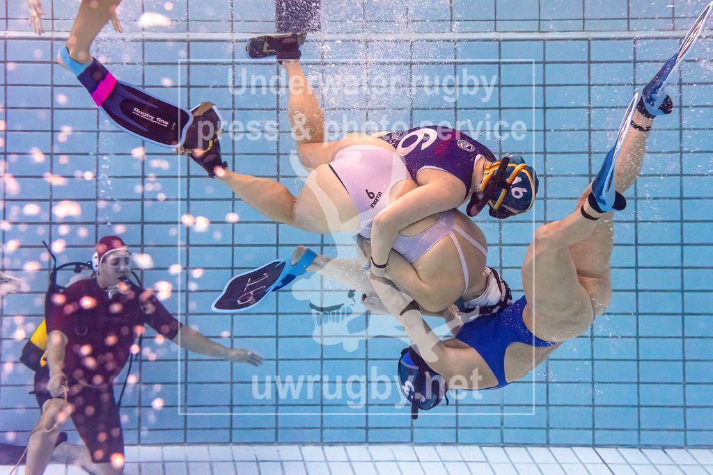 24. - 26.11.2023: Unterwasser-Rugby Champions Cup 2023  | Damen-Spiel um Platz 5:  Amager Uv-Rugby (Dänemark) in blau gegen UWRC Wien / Österreich in weiß. Die ballführende Ulrike Janovsky (weiß #9) wird von Klara Tetzscner Madsen (blau #16) und Louise Marie Lanng (blau #83) in der Spielfeldmitte gestoppt. - Realisiert mit Pictrs.com