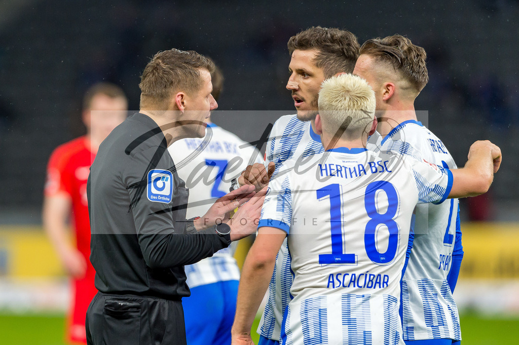 BSCRBL20220220_223 | Fussball, Herren: Schiedsrichter Patrick Ittrich, Stevan Jovetic (Hertha BSC), Peter Pekarik (Hertha BSC) und Santiago Ascacibar (Hertha BSC) diskutieren bei dem Spiel der 1. Bundesliga zwischen Hertha BSC und RB Leipzig im Olypiastadion am 20.02.2022 in Berlin, Deutschland.DFB / DFL REGULATIONS PROHIBIT ANY USE OF PHOTOGRAPHS AS IMAGE SEQUENCES AND/OR QUASI-VIDEO. - Realisiert mit Pictrs.com