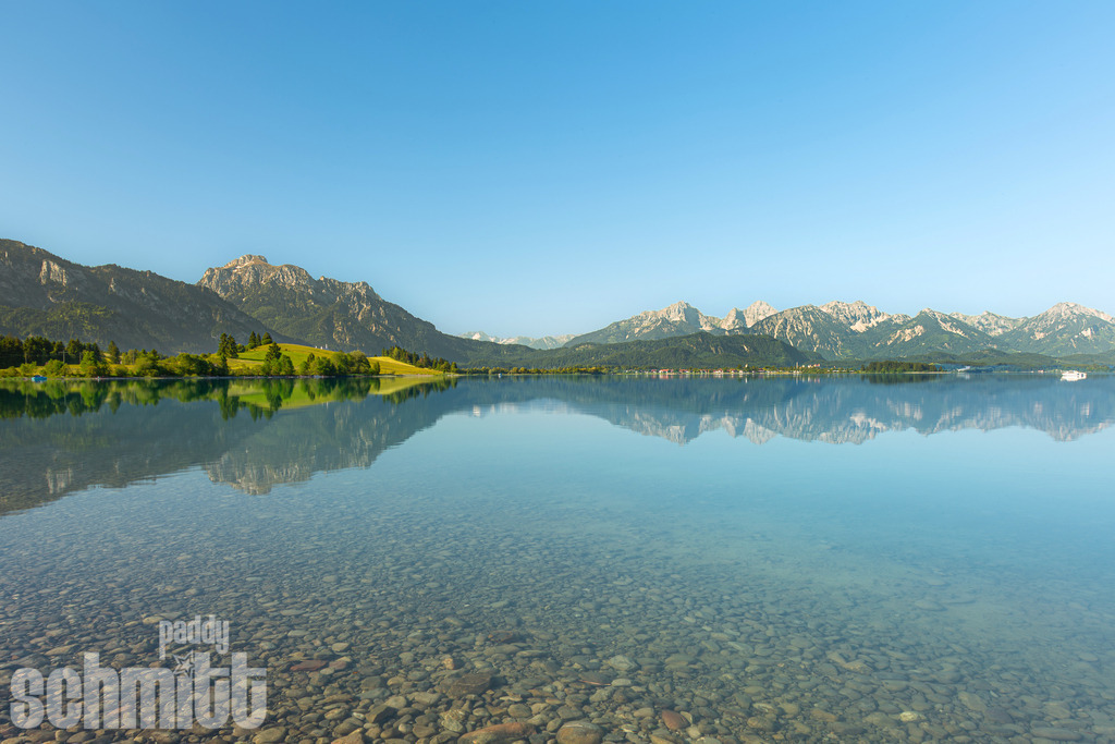 Forggensee im Sommer mit Wasserspiegelung | Sommerliche Stimmung am Forggensee mit beeindruckenden Wasserspiegelungen und der majestätischen Bergkulisse im Hintergrund. Ein idyllischer Moment voller Ruhe und Weite. - Realisiert mit Pictrs.com