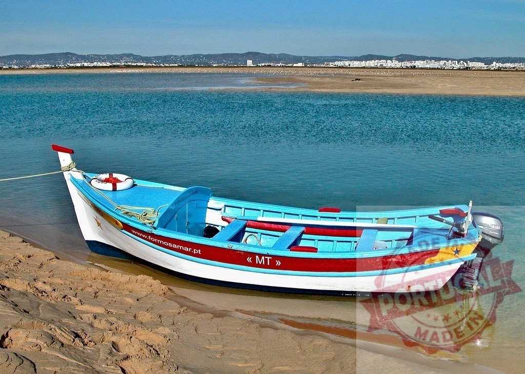 Traditional fishing boat resting on Ria Formosa sand | Colorful boat on the sand of Ria Formosa lagoon with turquoise water and distant cityscape - Realized with Pictrs.com