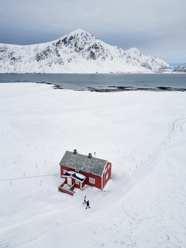 Einsame Hütte in der norwegischen Winterlandschaft | Eine rote Hütte steht allein in einer weiten, unberührten Schneelandschaft vor den Bergen Nordnorwegens. Die reduzierte Komposition vermittelt Ruhe, Weite und winterliche Abgeschiedenheit. - Realisiert mit Pictrs.com