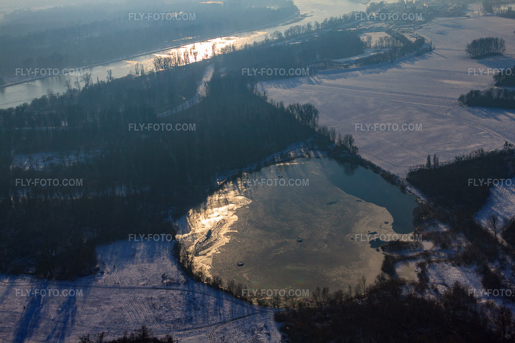Aerial view: Frozen quarry lake during winter snowfall in Lauterbourg in the state Bas-Rhin, France. – Photo: IMG_36566.jpg taken on 01/05/2011 by Werner Riehm/FLY-FOTO.com – Resolution of the original: 4752 x 3168 px