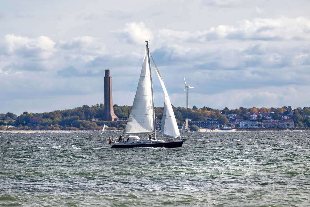 Wandbild: Segelboot auf der Kieler Förde vor Laboe | Dieses Wandbild im Querformat zeigt ein Segelboot auf der Kieler Förde vor Laboe. Das Foto wurde vom Strand in Strande mit Blick in Richtung Laboe aufgenommen. Im Hintergrund ist das Ehrendenkmal in Laboe zu sehen. Am Himmel befinden sich zahlreiche Wolken.  - Realisiert mit Pictrs.com