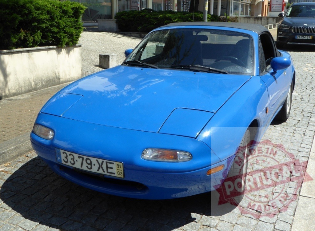 Mazda MX-5 NA Miata blue sports convertible parked | Blue Mazda MX-5 NA Miata sports convertible parked on cobblestone street - Realized with Pictrs.com