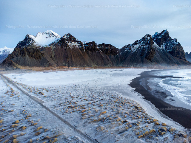 Schwarzer Strand vor Islands Bergen | Weite Winterlandschaft in Island mit schneebedeckten Bergen, schwarzem Sandstrand und ruhiger Küstenlinie. Die klare Kälte, die dunklen Felsen und der Kontrast zwischen Schnee und Vulkanstrand erzeugen eine eindrucksvolle nordische Atmosphäre. - Realisiert mit Pictrs.com