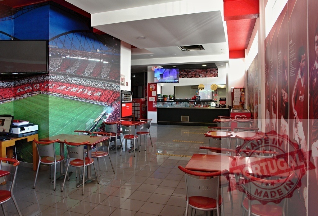 SL Benfica themed sports bar restaurant interior | Empty sports bar with red chairs and tables, featuring football stadium mural and club branding - Realisiert mit Pictrs.com