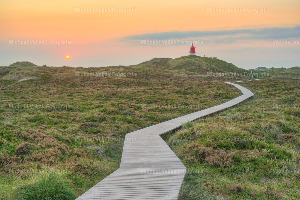 In den Dünen beim Quermarkenfeuer auf Amrum | Das Quermarkenfeuer auf Amrum, ein kleiner Leuchtturm im Nordwesten der Insel, ist ein bedeutendes Navigationszeichen für die Schifffahrt. Es steht auf einer Düne nahe der Vogelkoje und leitet mit seinen bunten Lichtern Schiffe sicher durch das Fahrwasser "Vortrapptief". Dieses historische Bauwerk, erbaut im Jahr 1906, erreicht mit seinem Licht eine Höhe von bis zu 22 Metern und bietet Besuchern eine malerische Aussichtsplattform. Ein Spaziergang zu diesem charmanten Leuchtturm, umgeben von der einzigartigen Dünenlandschaft Amrums, ist ein unvergessliches Erlebnis. - Realisiert mit Pictrs.com