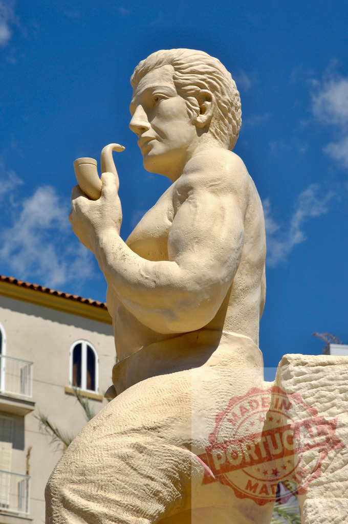 Stone man statue holding pipe against blue sky. Provincia Castellon - Spain | Stone sculpture depicting a man holding a pipe in profile outdoors - Realisiert mit Pictrs.com