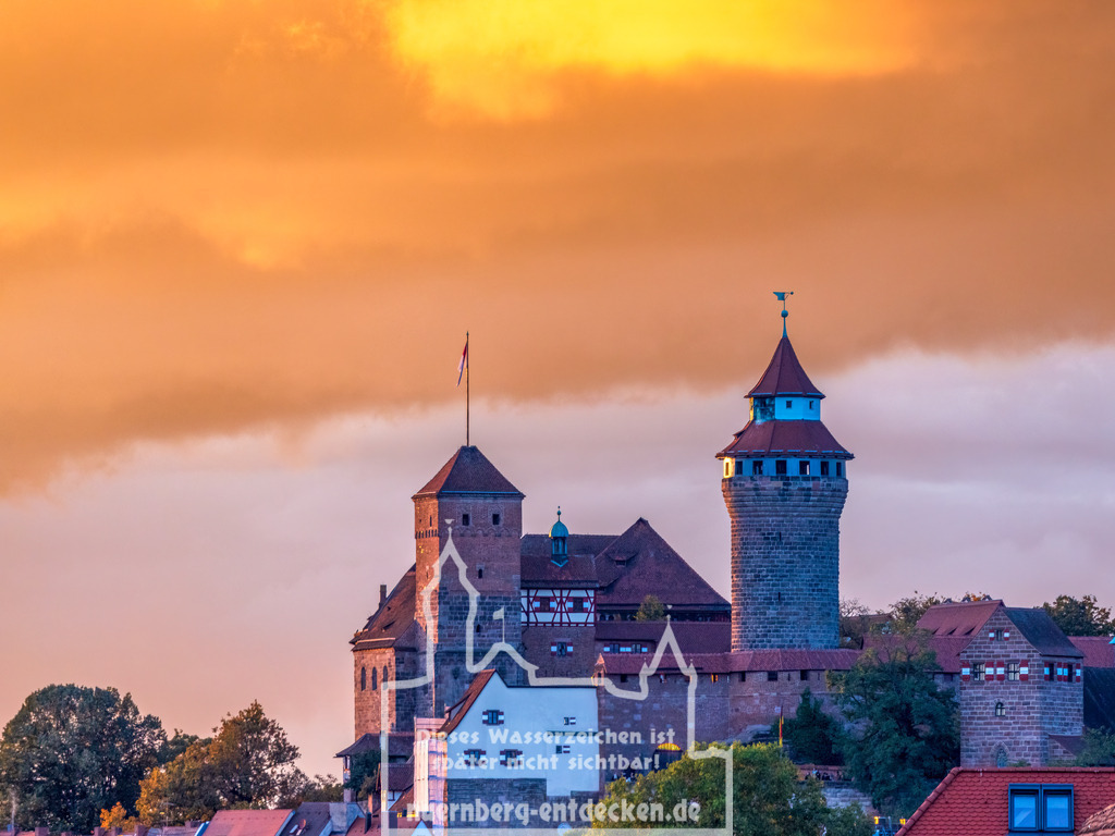 Monatsbild des Kalender 2025 für den Monat November | Die Nürnberger Kaiserburg im warmen Licht eines herbstlichen Sonnenuntergangs. Die mittelalterlichen Türme und Mauern der Burg heben sich eindrucksvoll gegen den orangefarbenen Himmel ab, der von den letzten Strahlen der untergehenden Sonne beleuchtet wird. - Realisiert mit Pictrs.com