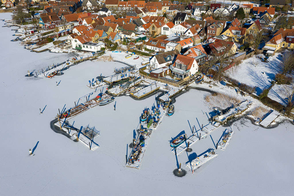 deutschland-2021-010 | Im Eis der Schlei: Landungsbrücken und Boote in der Fischersiedlung Holm in Schleswig aus der Vogelperspektive - Realisiert mit Pictrs.com