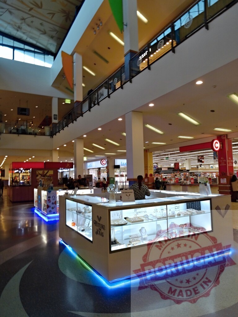 Jewelry kiosk in modern shopping mall interior | Jewelry kiosk displaying products in a busy shopping mall with retailers and customers - Realized with Pictrs.com
