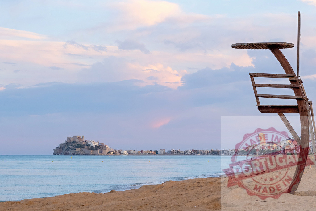 Lifeguard chair standing on Peñíscola beach at sunset | Lifeguard chair on sandy beach with Peñíscola castle and town across the bay - Realized with Pictrs.com