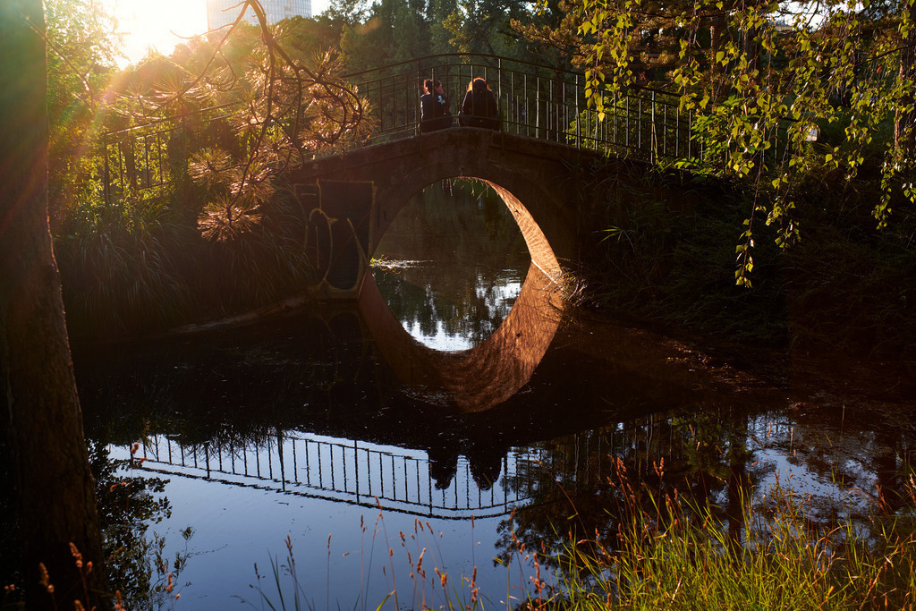 Brücke mit zwei Menschen im Wasserpark | Wien, Austria - June 29, 2020: Brücke im Floridsdorfer Wasserpark mit zwei Menschen im Abendlicht. - Realisiert mit Pictrs.com