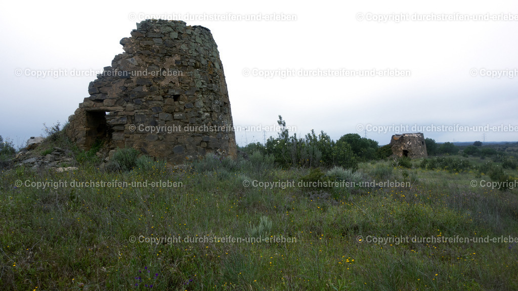 Verfallende Windmühlen am Megalithgrab Anta da Masmorra, Mealha, Algarve | In der Nähe des traditionellen Dorfes Mealha,Gemeinde Tavira, im Hinterland der Algarve befinden sich bedeutende prähistorische Fundstätten, die vor allem über Wanderwege erschlossen sind. Das bekannteste Monument in dieser Gegend ist die Anta da Masmorra.Dieses Megalithgrab, Dolmen, ist eines der am besten erhaltenen Beispiele seiner Art in der östlichen Algarve-Region, genauer Serra do Caldeirão. Es handelt sich um eine megalithische Grabkammer (Anta), bestehend aus mehreren aufrecht stehenden Steinen und einem Deckstein. Sie liegt auf einem Hügel etwa zwei Kilometer von Mealha entfernt und bietet einen weiten Blick über die Hügellandschaft. Die Anta ist Teil des Rundwanderwegs PR8 TVR, Mascarra-Trail, der in Mealha beginnt. Die Strecke ist etwa 5,4 km lang und als leicht eingestuft. - Realisiert mit Pictrs.com