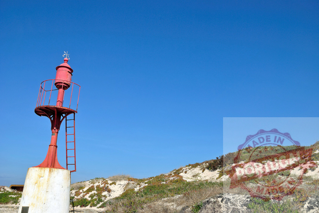 Red beacon standing on sand dunes with clear blue sky. Centro - Portugal | Red beacon providing coastal navigation on sandy dunes under a clear blue sky - Realisiert mit Pictrs.com
