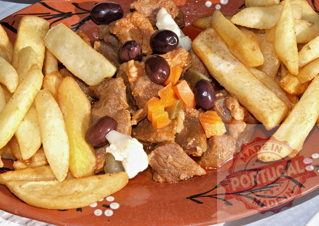 Pica pau Portuguese pork delicacy with french fries | Pica pau with marinated pork, pickles, olives, and crispy french fries on a traditional plate - Realized with Pictrs.com