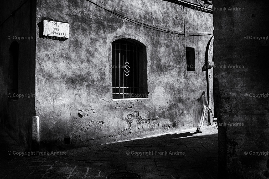 Nonne in Siena | Eine ältere Nonne mit Gehstock geht durch die Altstadt von Siena. Die Sonne wirft lange Schatten. Straßenfotografie aus Italien  in schwarz weiß. - Realisiert mit Pictrs.com