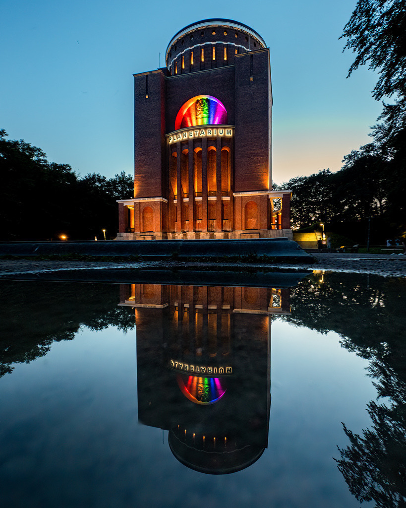 Planetarium Hamburg in Regenbogenfarben mit Spiegelung | Das Planetarium Hamburg in farbenfroher Pride-Beleuchtung, gespiegelt im Wasserbecken des Hamburger Stadtparks. - Realisiert mit Pictrs.com