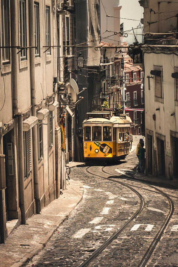 Linie 28 – Straßenbahn in Lissabon | Mit quietschenden Rädern schlängelt sich die legendäre Linie 28 durch die engen Gassen der Altstadt von Lissabon. Die gelbe Straßenbahn ist mehr als ein Verkehrsmittel – sie ist ein Stück gelebte Geschichte, Symbol der Stadt und Lieblingsmotiv für Reisende aus aller Welt. Dieses Bild fängt das einzigartige Flair portugiesischer Straßen ein: voller Charme, Leben und Nostalgie. - Realisiert mit Pictrs.com