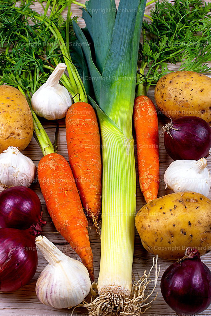 Gemüse-Sortenmix | Auf einem Holzgrund liegt eine Gemüsemischung aus Lauch, Zwiebeln, Knoblauch, Kartoffeln und Karotten. - Realisiert mit Pictrs.com