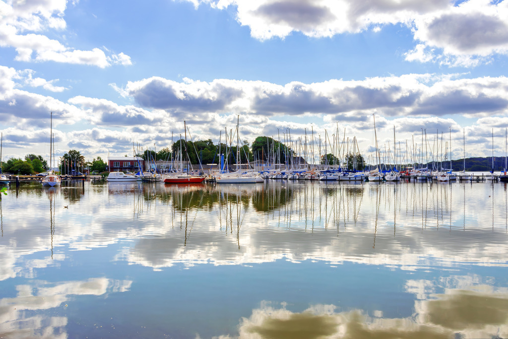Leinwand: Spiegelung auf der Schlei in Schleswig | Dieses Wandbild im Querformat zeigt den Yachthafen in Schleswig. Auf der Schlei ist eine schöne Spiegelung zu sehen. Am blauen Himmel befinden sich einige sommerliche Wolken.  - Realisiert mit Pictrs.com