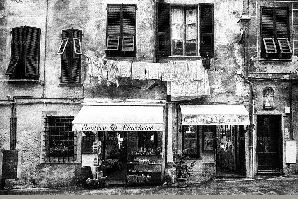 Alte Hausfassade Italien | Eine typische Hausfassade aus einer italienischen Altstadt. Über Einkaufsläden hängt Wäsche an einer Wäscheleine.
Straßenfotografie aus Italien in schwarz und weiß - Realisiert mit Pictrs.com
