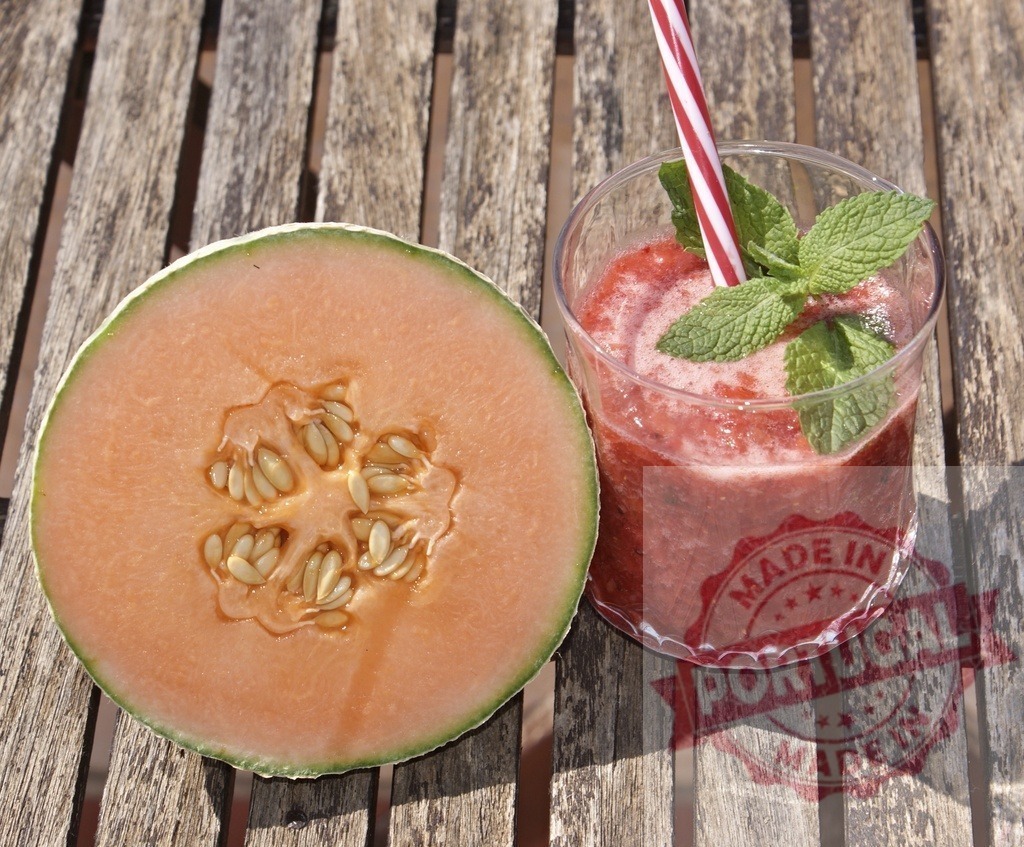 Refreshing melon smoothie for a healthy summer drink | Melon half beside a fresh red fruit smoothie with mint and striped straw on wooden table - Realisiert mit Pictrs.com