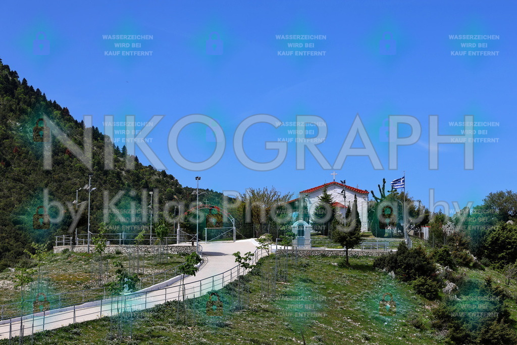 Profitis Ilias Kapelle - Epirus, Griechenland | Eine malerische orthodoxe Kapelle des Propheten Elias (Profitis Ilias) in der bergigen Landschaft von Epirus, Griechenland. Das weiße Gebäude mit rotem Ziegeldach und wehender griechischer Flagge thront auf einer grünen Anhöhe und bietet einen weitreichenden Blick über die bewaldeten Täler der Präfektur Ioannina. Ein authentisches Motiv, das die Ruhe und Spiritualität der griechischen Bergwelt einfängt – ideal für hochwertige Wandbilder, Kalender und Reise Publikationen.