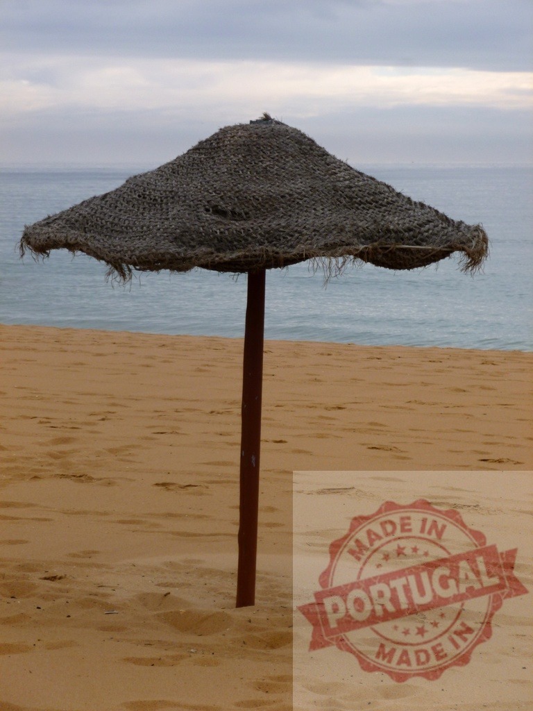 Straw parasol standing on an empty beach | Straw parasol standing on sand with ocean and cloudy sky in the background, symbolizing solitude - Realized with Pictrs.com