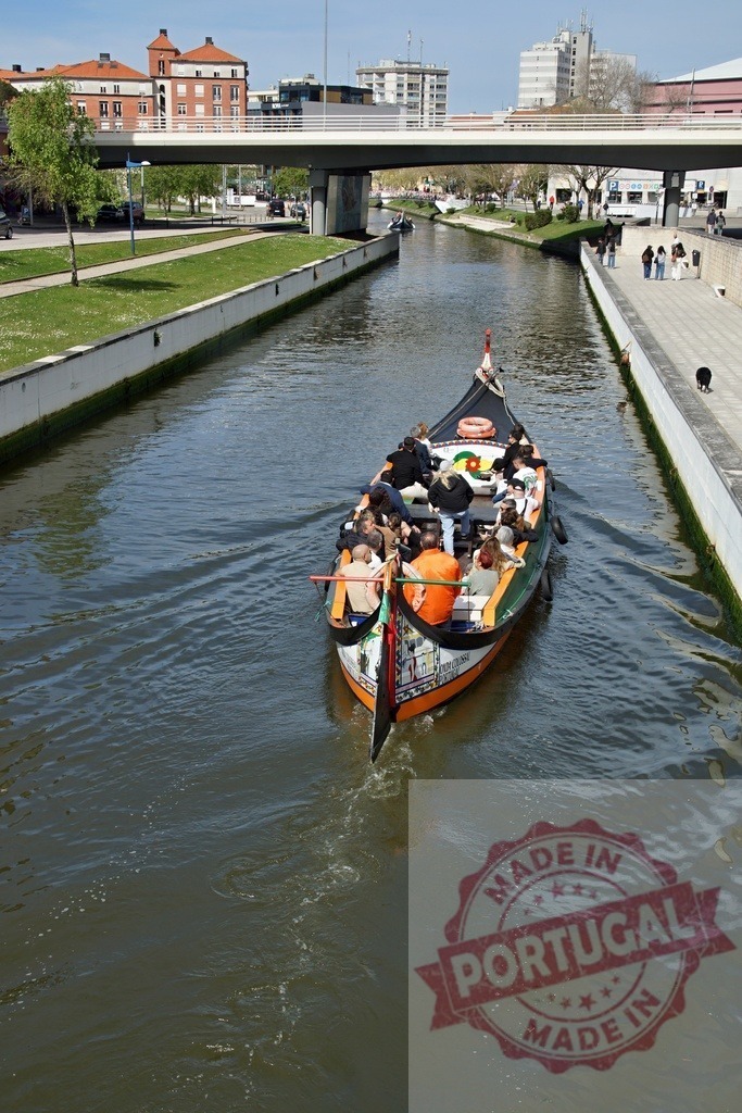 Moliceiro boat cruising Aveiro canal with tourists. Aveiro - Portugal | Moliceiro boat carrying tourists along an urban canal with city buildings and a bridge - Realized with Pictrs.com