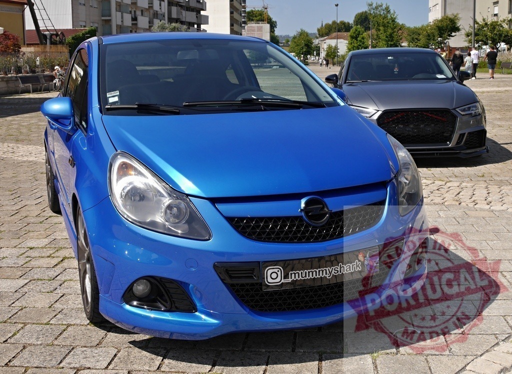 Blue Opel Corsa and Audi A3 street meet | Blue Opel Corsa and gray Audi A3 parked on cobblestones at a street car meet - Realized with Pictrs.com