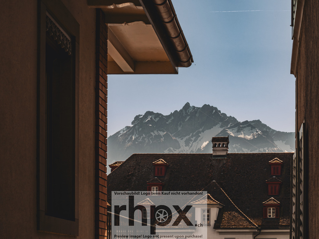 Luzern Altstadt mit Pilatus – Blick durch Gasse | Blick durch eine enge Gasse der Luzerner Altstadt auf ein historisches Gebäude mit dem Pilatus im Hintergrund.  - Realisiert mit Pictrs.com