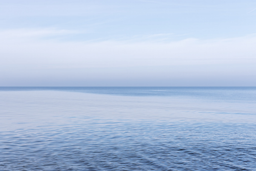 Weite Wasserfläche unter klarem Himmel – Minimalistische Meeresfotografie | Eine ruhige, weit ausgedehnte Wasserfläche trifft auf einen klaren Himmel und schafft ein reduziertes, kraftvolles Motiv voller Stille. Die sanften Wellenstrukturen und die feine Horizontlinie verleihen dem Bild eine subtile Dynamik, die dennoch vollkommen beruhigend wirkt. Die minimalistische Komposition öffnet Räume optisch und bringt eine Atmosphäre von Klarheit, Leichtigkeit und zeitloser Eleganz in moderne Interiors. Dieses Fine‑Art‑Wandbild setzt einen hochwertigen, puristischen Akzent und eignet sich ideal für Wohnbereiche, Arbeitsräume oder Orte, die bewusst Ruhe und Fokus ausstrahlen sollen.