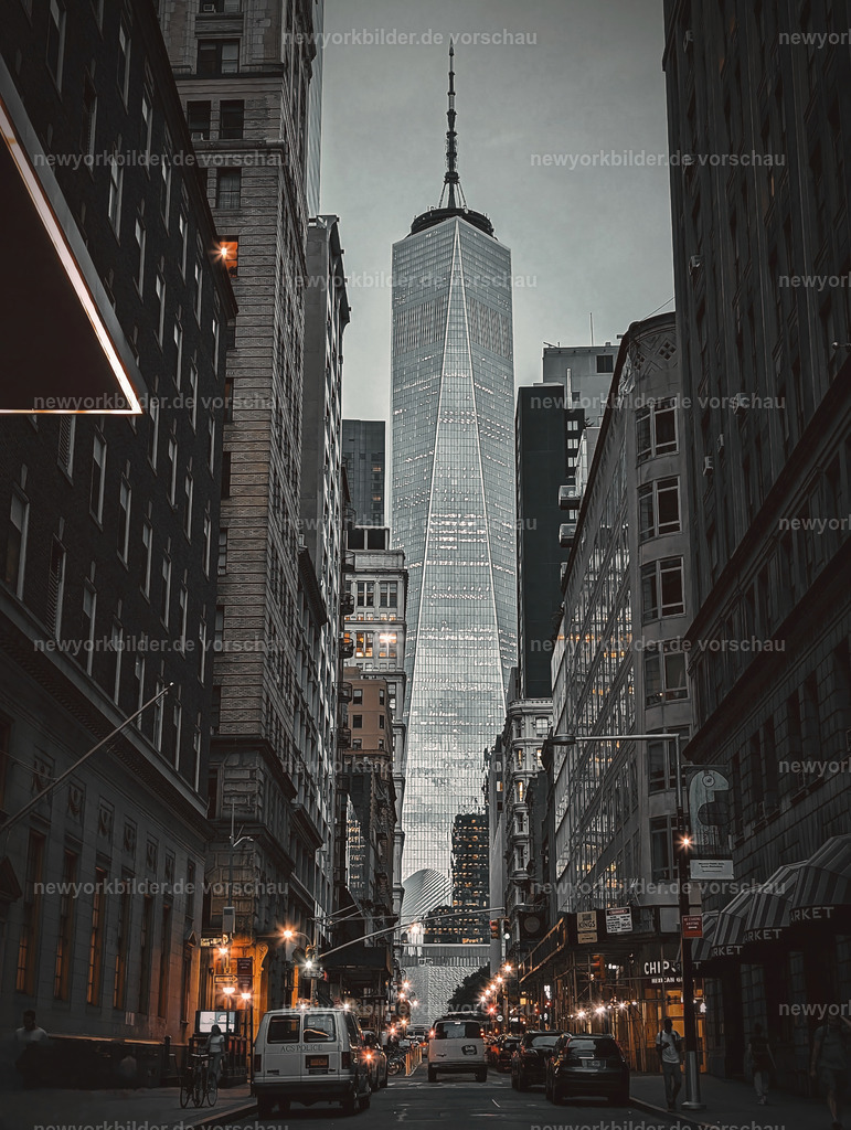 Zwischen den Straßen von Manhattan erhebt sich das One World Trade Center | Die Straßen von Manhattan wirken wie ein Labyrinth aus Licht und Schatten, und zwischen ihnen erhebt sich das One World Trade Center – mächtig, dominant und voller Symbolkraft. Der Himmel verdunkelt sich, die ersten Lichter gehen an, und die Fassaden der Wolkenkratzer spiegeln die letzten Spuren des Tageslichts. Eine düstere, fast dramatische Stimmung liegt über der Stadt, die zugleich Faszination und Ehrfurcht weckt. Der Blickwinkel zwischen den Hochhäusern lässt die Dimensionen spürbar werden: Hier ist alles größer, schneller, intensiver. Es ist ein Moment, der die Energie New Yorks einfängt und zeigt, warum diese Stadt niemals langweilig wird.