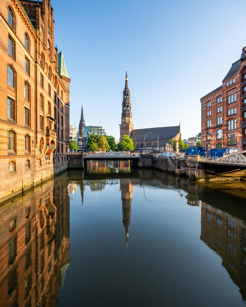 Fleetblick in der Speicherstadt mit Kirchturm | Ruhiger Blick entlang eines Fleets in der Hamburger Speicherstadt mit stimmungsvoller Spiegelung und Kirchturm im Hintergrund. - Realisiert mit Pictrs.com