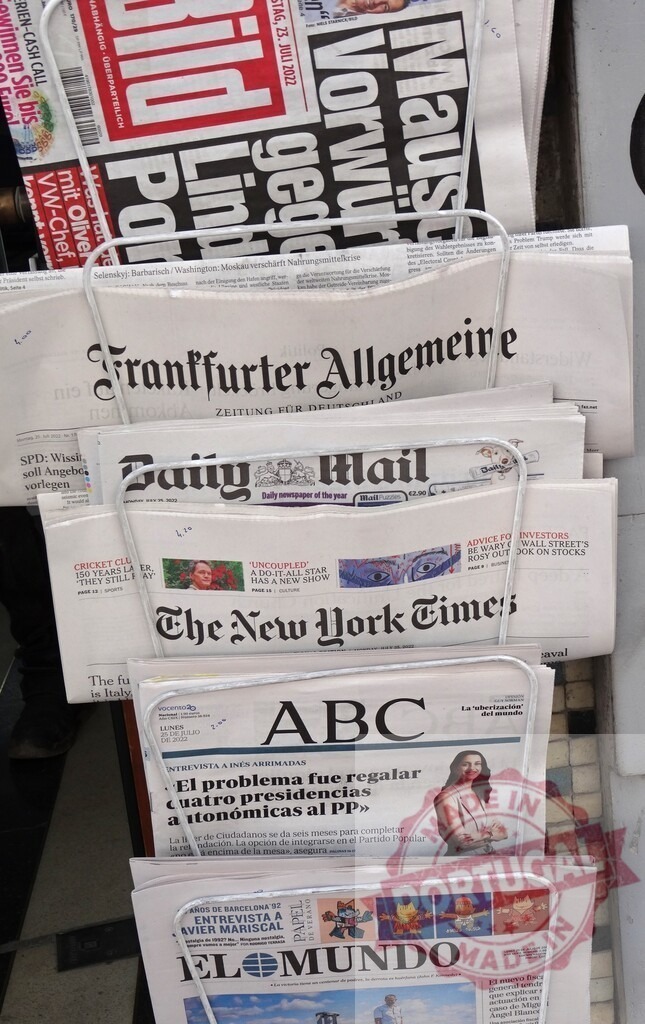 International newspapers displayed on newsstand presenting diverse global perspectives | Various international newspapers from different countries are neatly arranged on a newsstand, offering a glimpse into current events and diverse perspectives from around the world - Realisiert mit Pictrs.com