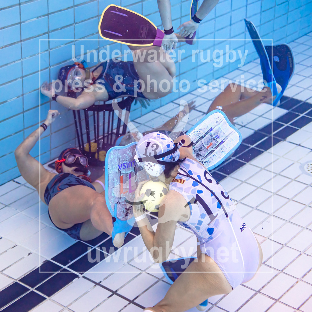 24. - 26.11.2023: Unterwasser-Rugby Champions Cup 2023  | Damen-Spiel: NJ Hammerheads (USA) in blau gegen Barcelona (Spanien) in weiß. Marta Bercianos de la Salud (weiß #13) wird von der amerikanischen Verteidigung mit ausgestreckten Füßen vom Tor ferngehalten. - Realisiert mit Pictrs.com