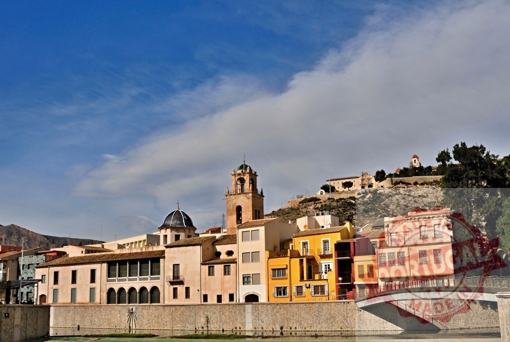Orihuela cityscape with Segura river and historical buildings | Orihuela cityscape showcasing historic architecture, colorful facades, and the Segura River under a blue sky - Realized with Pictrs.com